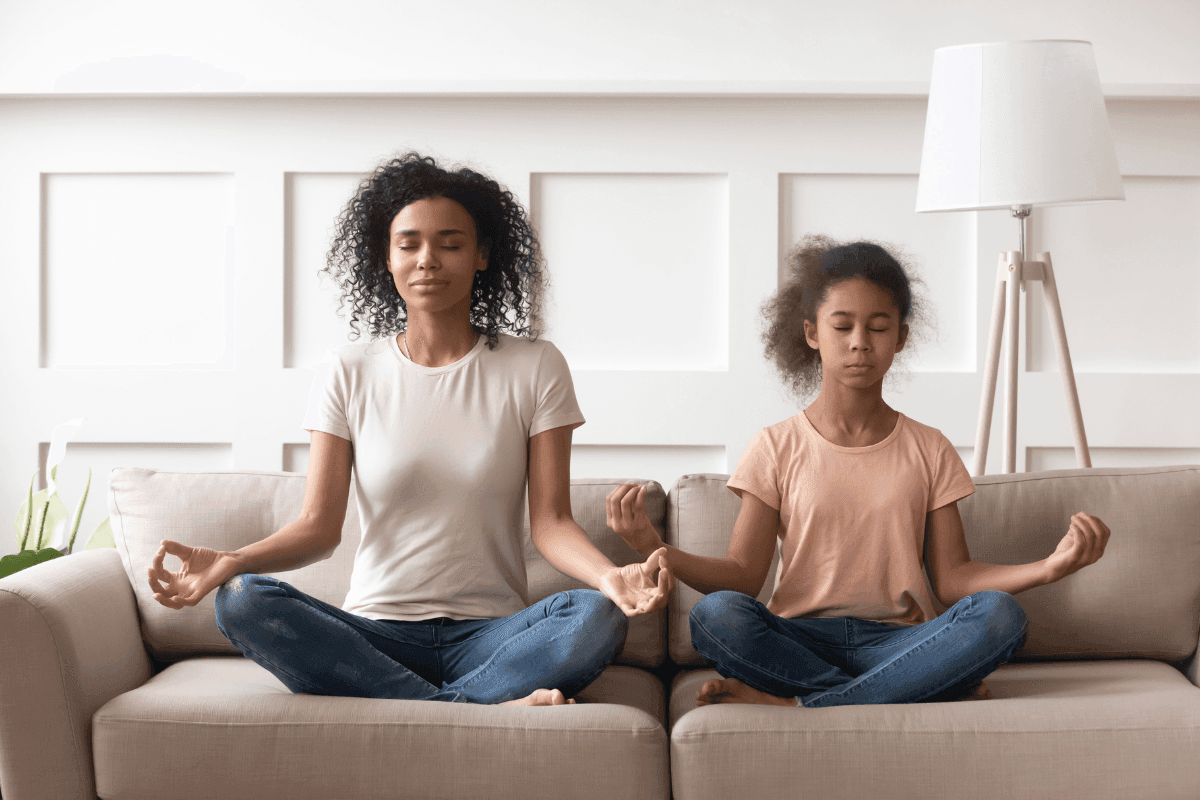 Mother and daughter meditating on couch at home